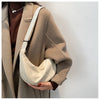 A woman wearing a beige coat is holding a cream-colored sling crossbody bag.