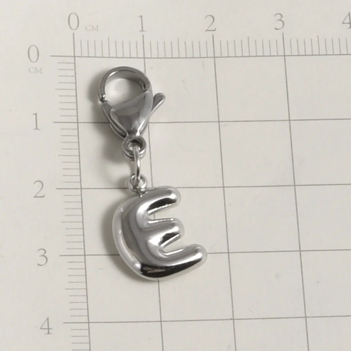 Silver stainless steel alphabet letter charm with a lobster clasp shown against a ruler.