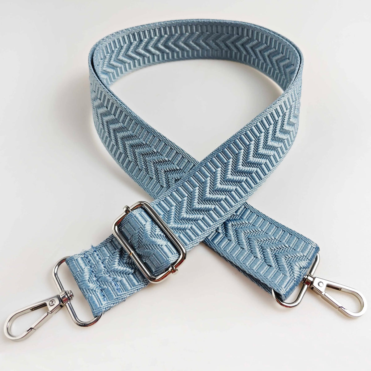 A light blue woven strap with an arrow jacquard pattern, shown crossed on a white background.