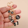 A gold enamel heart keychain with a black bow and the number five is held in a hand.