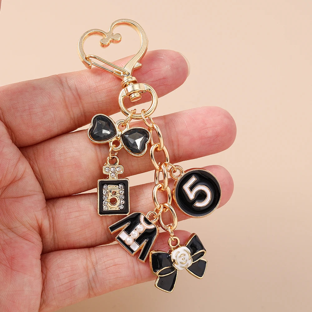 A gold enamel heart keychain with a black bow and the number five is held in a hand.