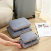A hand is placing a stack of gray travel compression packing cubes onto a wooden surface next to a radiator.