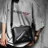 A person holds a black embossed crossbody clutch bag featuring a replica firearm design.