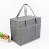 A gray foldable insulated grocery and food cooler bag with handles, shown next to some pink flowers.