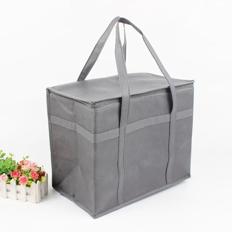 A gray foldable insulated grocery and food cooler bag with handles, shown next to some pink flowers.