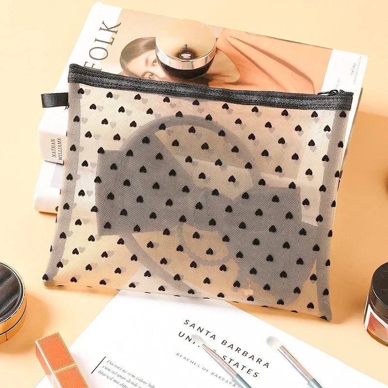 A clear mesh cosmetic storage pouch with a black and white heart pattern is shown next to a magazine.