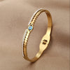 Gold cuff bracelet featuring a textured band and an evil eye crystal charm.
