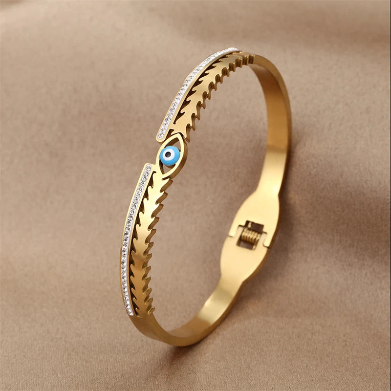 Gold cuff bracelet featuring a textured band and an evil eye crystal charm.