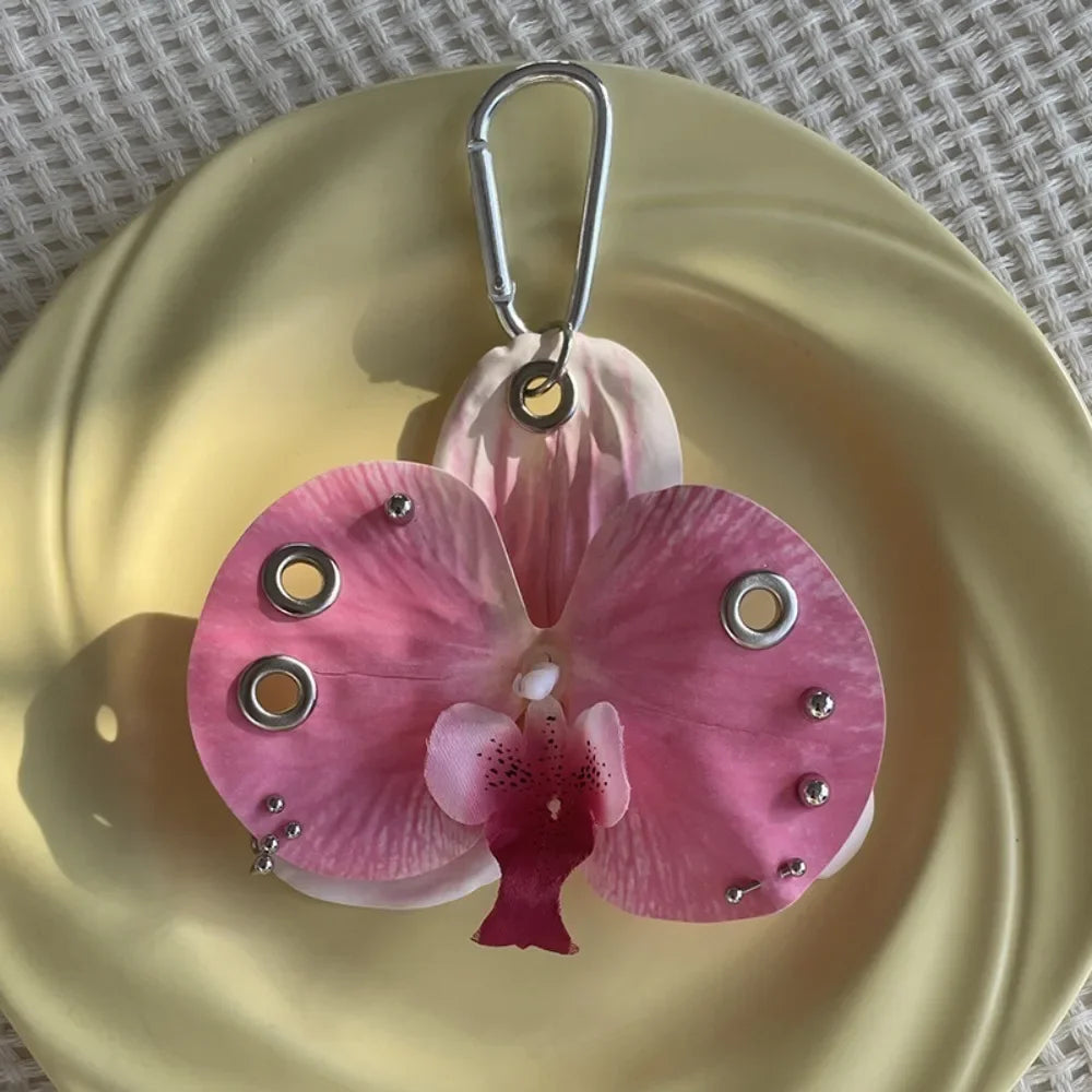 A realistic pink phalaenopsis orchid flower keychain hanging from a silver loop, displayed on a gold plate.