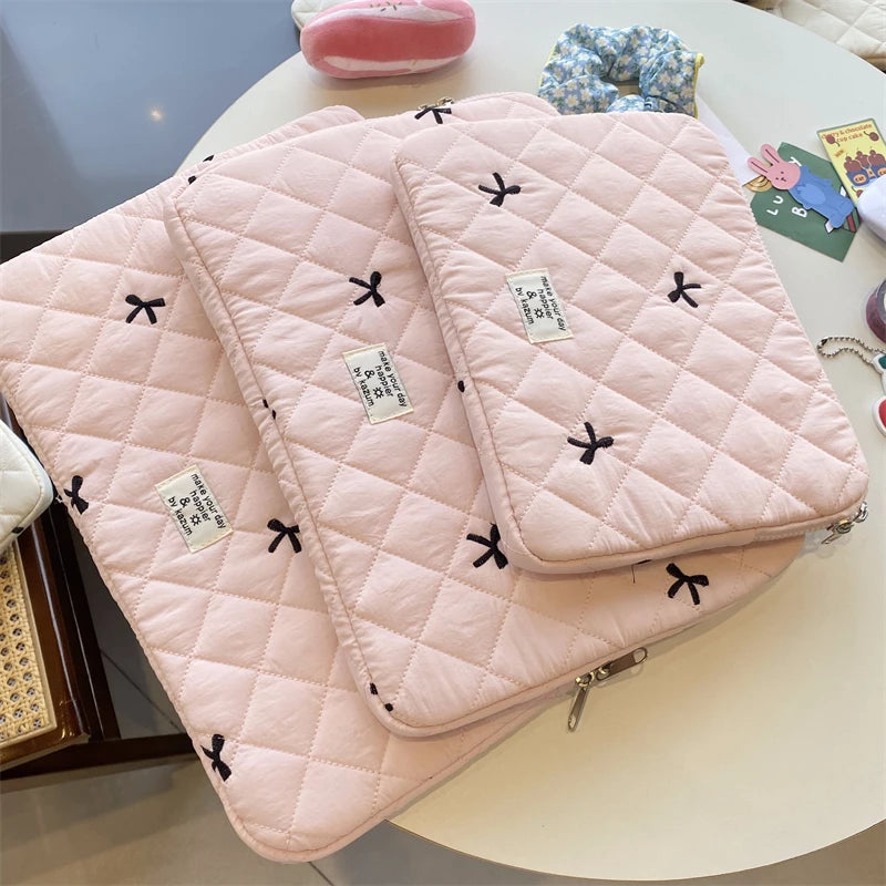 A stack of pink quilted slim laptop sleeves for MacBook and tablet placed on a white table.