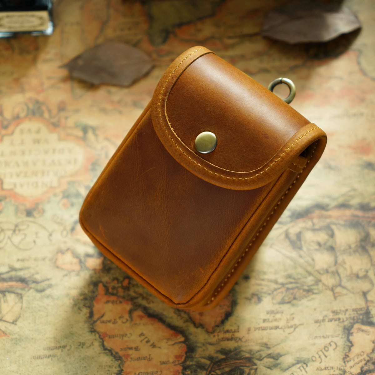 A brown leather men's multi-functional waist bag resting on an old map.