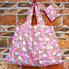 A pink and white patterned reusable shopping bag hanging against a brick wall.