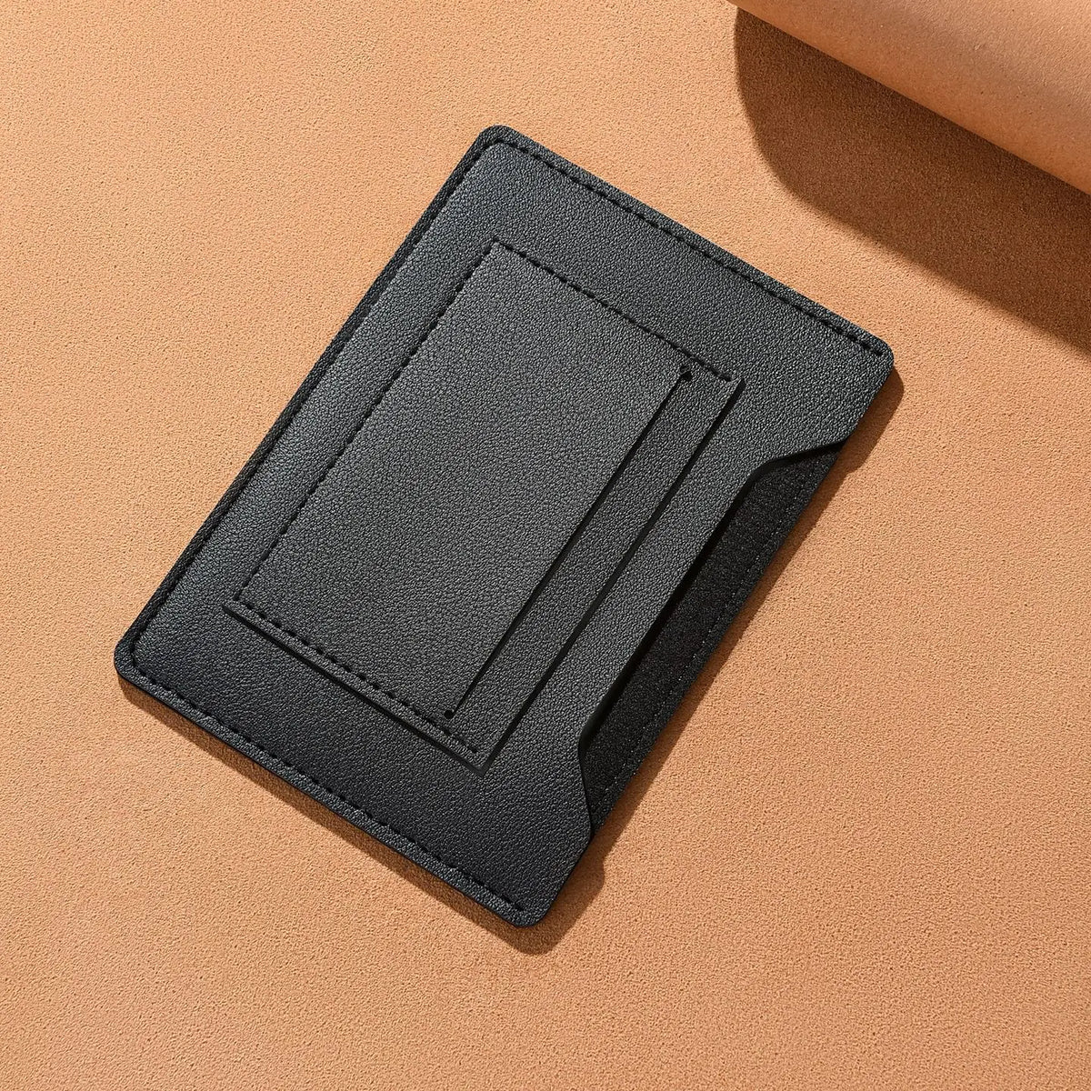 Portefeuille de voyage noir et fin, conçu pour contenir un passeport et des documents, montré sur une surface beige.