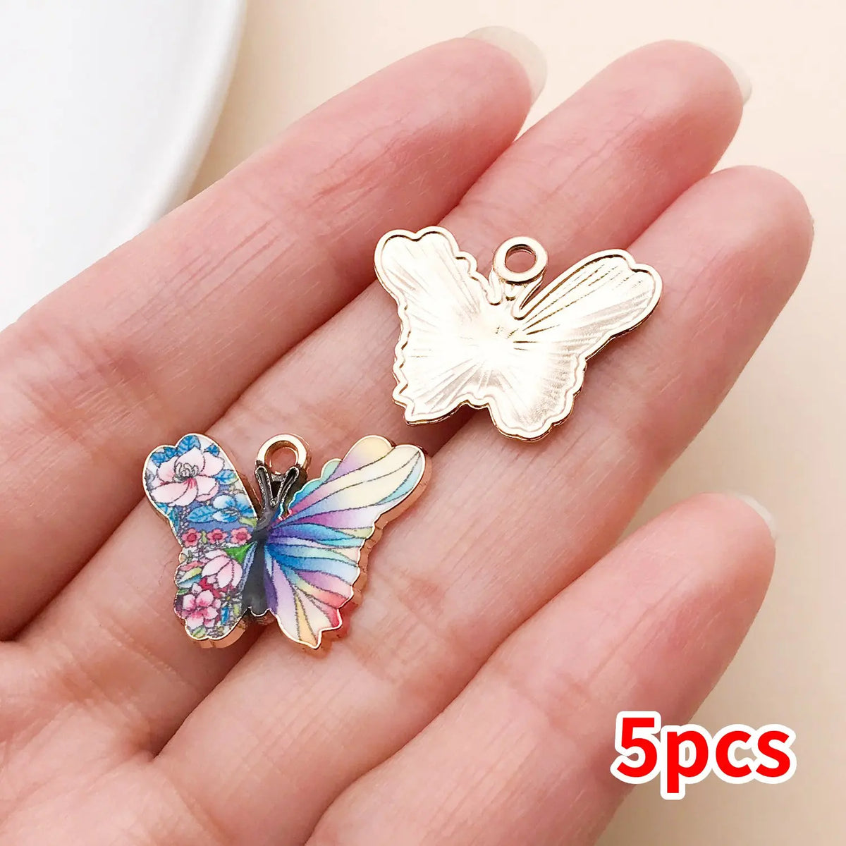A hand holds a set of five colorful butterfly enamel charms on a light background.
