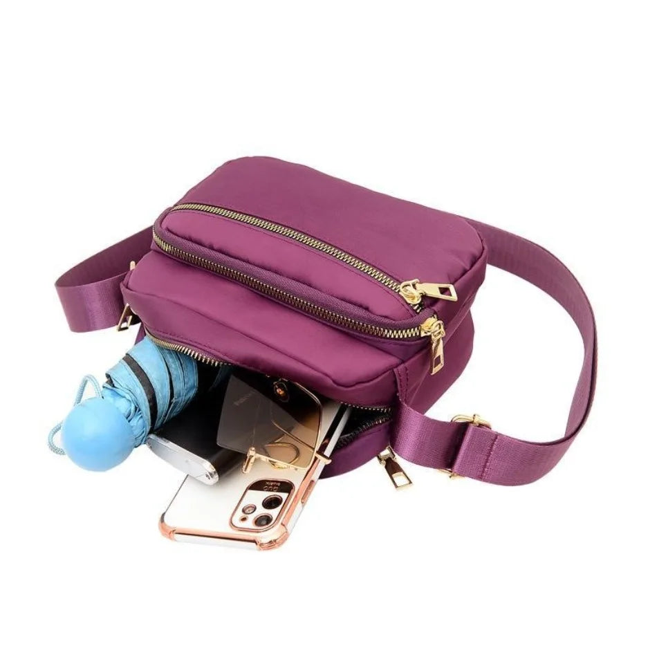 A purple compact oxford fabric crossbody bag with a gold zipper and a light blue strap.