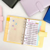 A yellow budget sheet inside an A7 crocodile ring binder notebook with pink and blue accessories.
