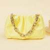 Cartera de acrílico amarillo pálido con correa de cadena dorada sobre un fondo claro.