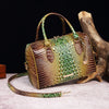 A luxury crocodile pattern crossbody tote bag with leather handles rests on a light surface next to a piece of driftwood.