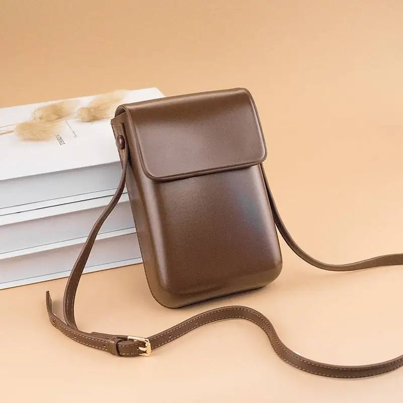 A brown vintage PU leather crossbody bag with an adjustable strap resting on a stack of white papers.