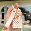 A hand holds a pink silicone heart beach bag keychain with a gold ring.