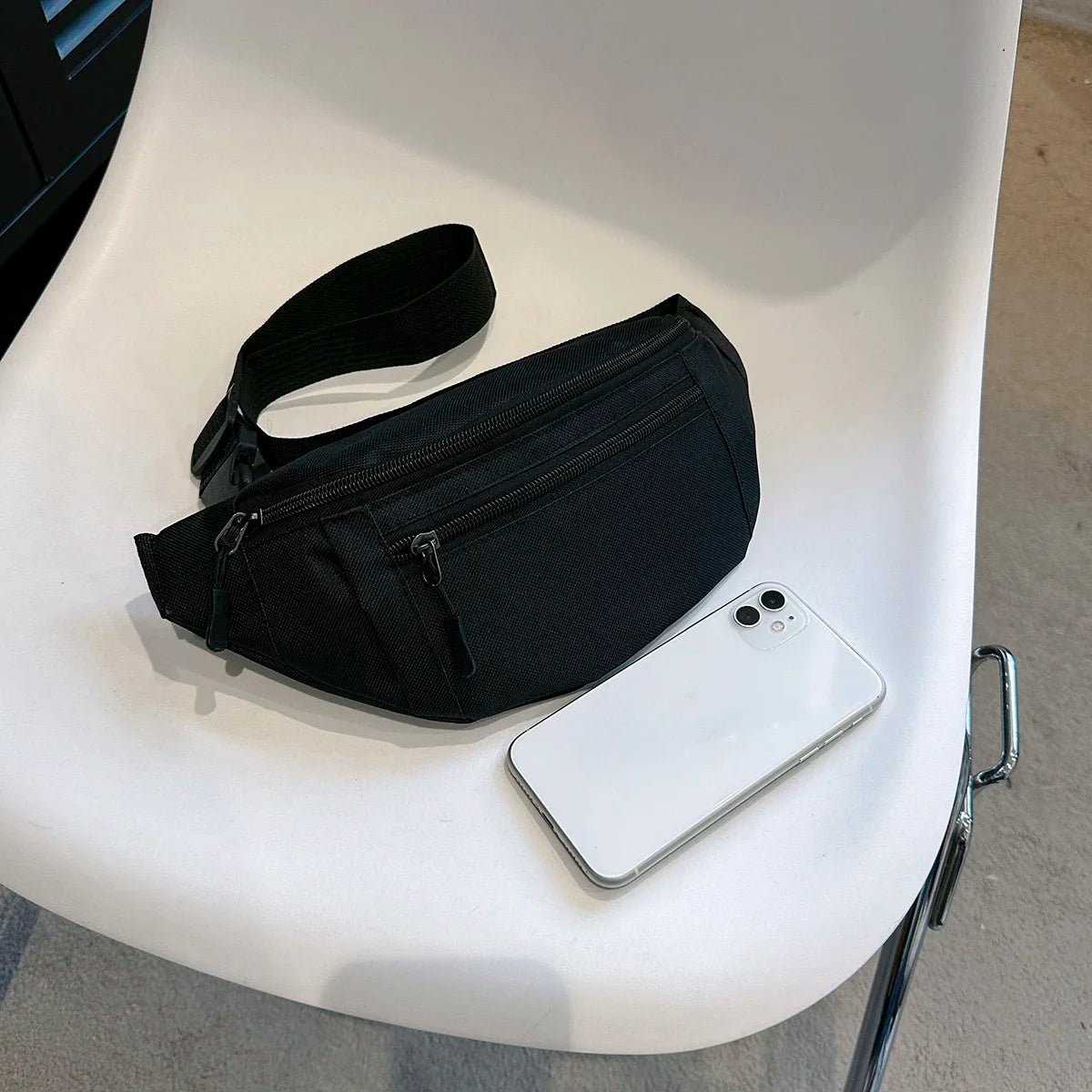A black compact nylon waist bag is placed on a white table next to a white smartphone.