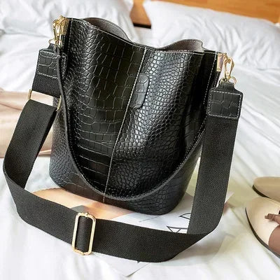 Black vintage alligator pattern leather crossbody bag resting on white bedding.