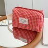 A red and white plaid cosmetic storage bag with a light pink strap is shown resting on a round mirror.