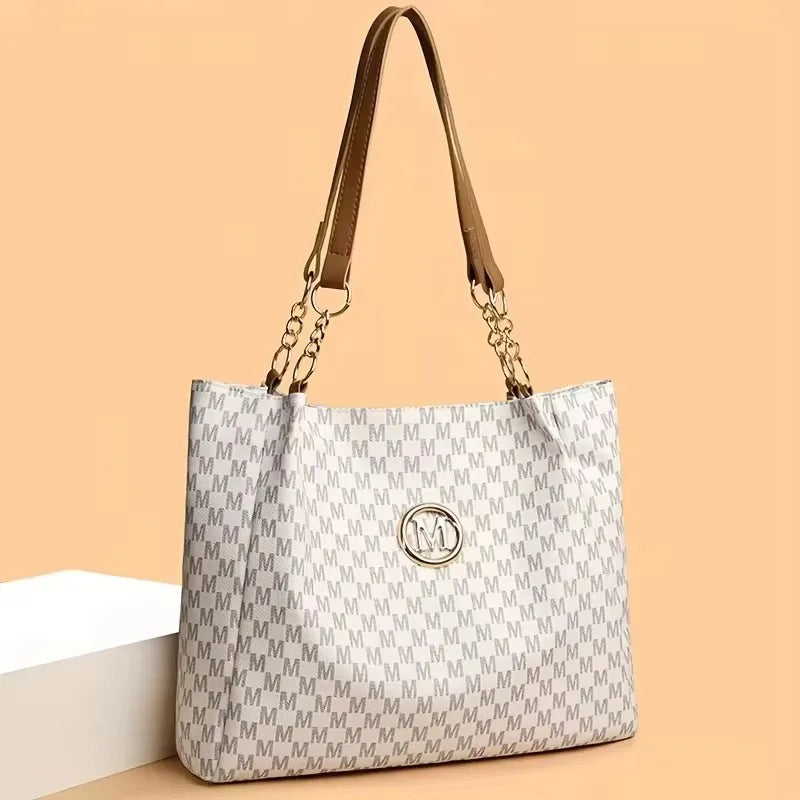 A beige and white geometric letter M tote bag with tan leather handles displayed on a white surface.