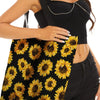 A woman holds a black sunflower canvas tote bag with yellow sunflowers against her torso.