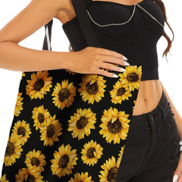 A woman holds a black sunflower canvas tote bag with yellow sunflowers against her torso.