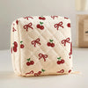A cream quilted storage pouch featuring a red cherry and bow print.