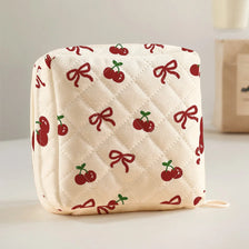 A cream quilted storage pouch featuring a red cherry and bow print.