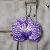 A purple orchid flower keychain with silver hardware attached to a gray fabric pocket.