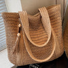 A natural straw woven tote bag with a wide strap is shown in a close-up view.
