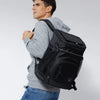 A man wearing a grey sweatshirt is holding an insulated thermal cooler backpack.