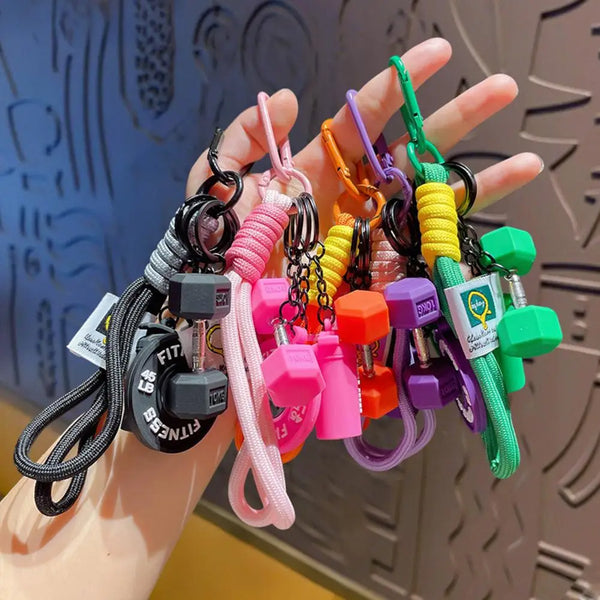 A hand holds a collection of colorful fitness keychains featuring dumbbell and kettlebell charms.