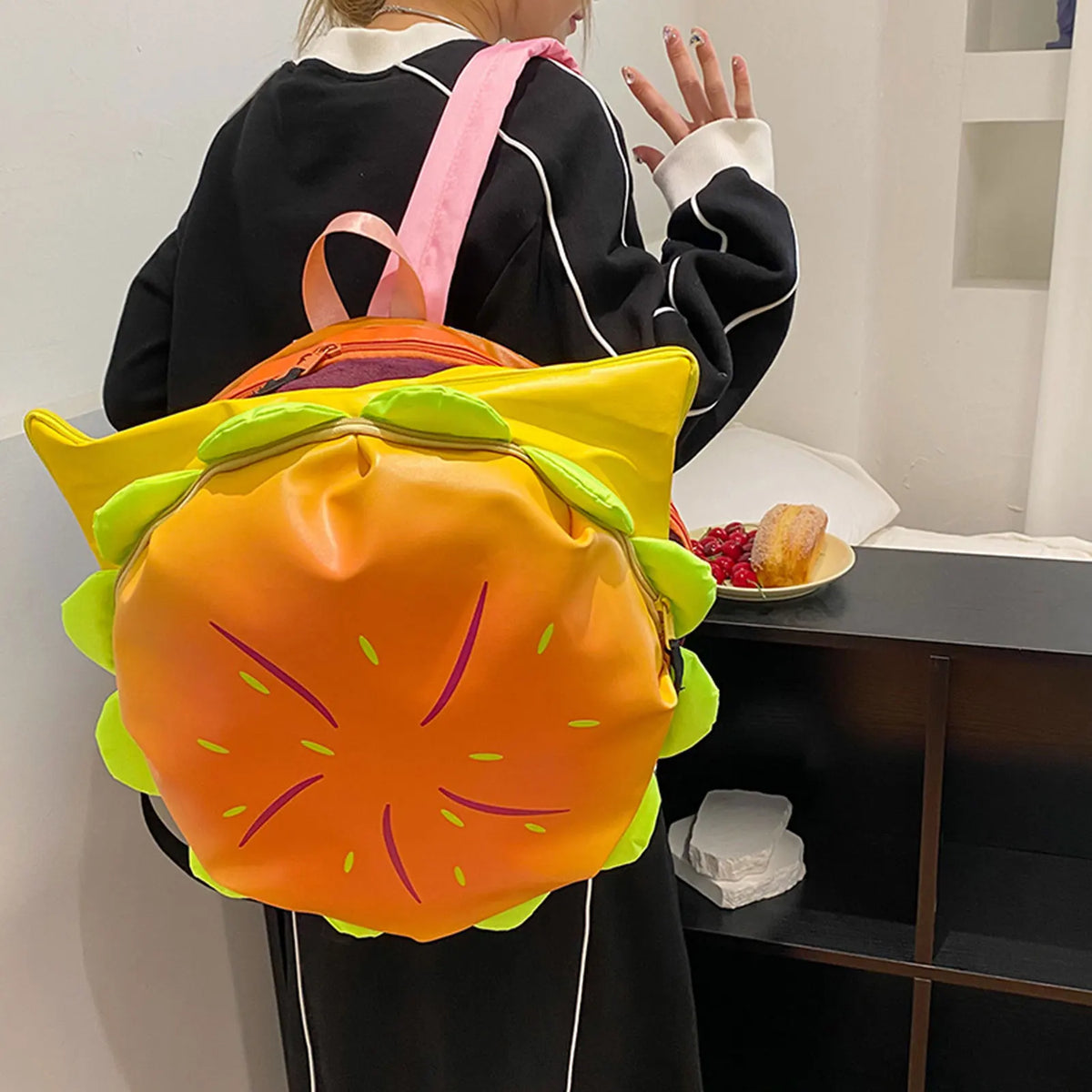 A person is holding a bright orange and green novelty backpack shaped like a cheeseburger.