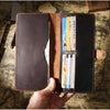 A hand holds open a genuine leather long bi-fold wallet with a snap closure, displaying various cards inside.