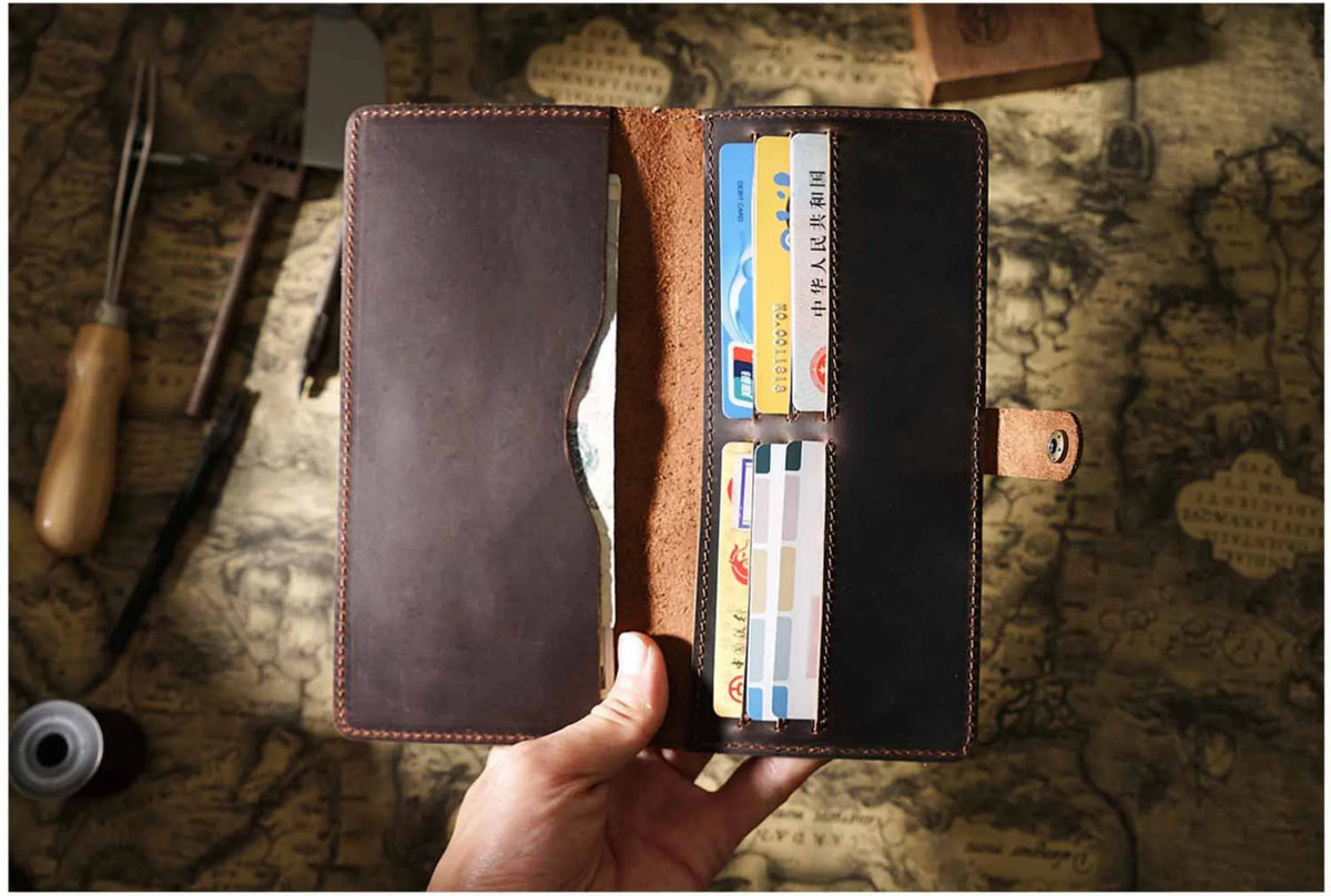 A hand holds open a genuine leather long bi-fold wallet with a snap closure, displaying various cards inside.