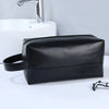 A black portable PU leather cosmetic organizer bag resting on a white surface next to a sink.