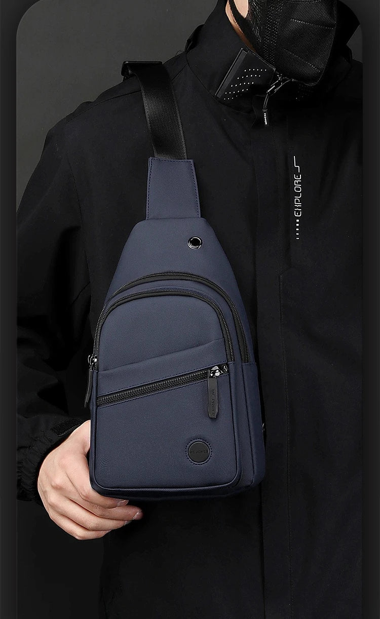 A navy blue lightweight nylon crossbody sling bag is shown being held by a person against a black jacket.