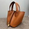 A brown classic genuine leather bucket bag with a gold clasp is shown on a gray surface.