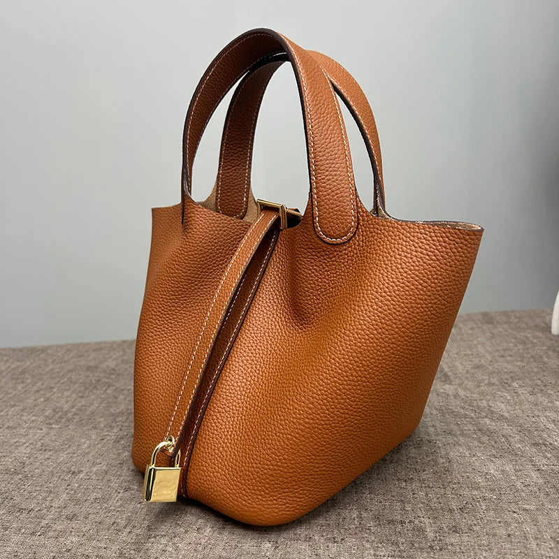 A brown classic genuine leather bucket bag with a gold clasp is shown on a gray surface.