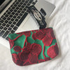 A deep red floral embroidered pouch with green fabric resting on a silver laptop.