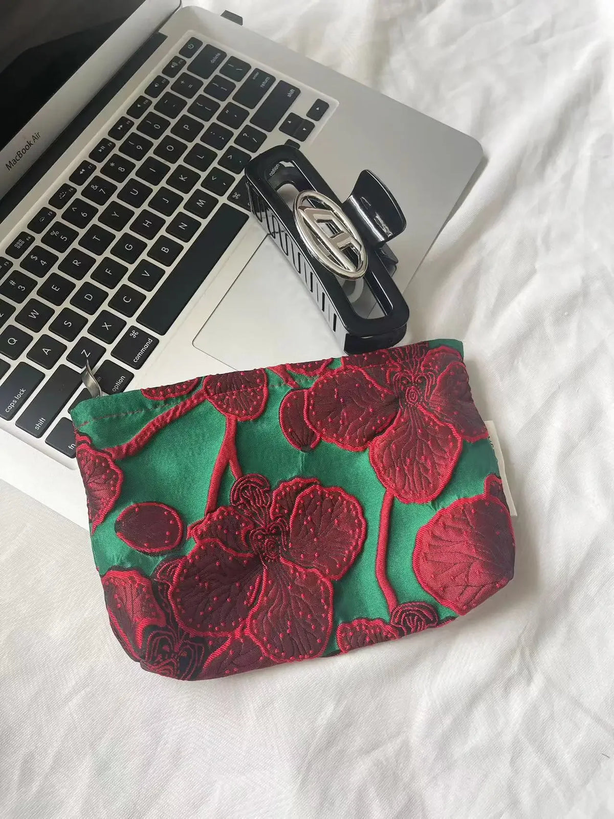 A deep red floral embroidered pouch with green fabric resting on a silver laptop.