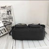A black nylon crossbody bag is displayed on a white surface next to a stack of magazines and a wire basket.