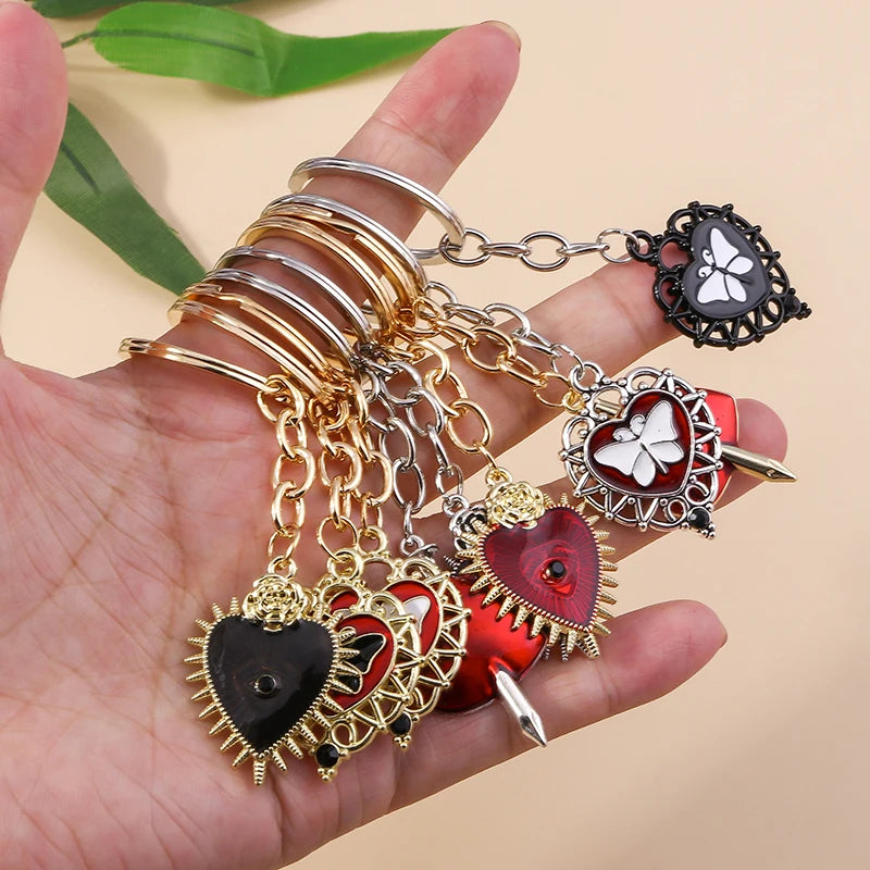 A hand holds a set of gold and silver chains with heart-shaped pendants, including a black heart and a red heart with a sun e