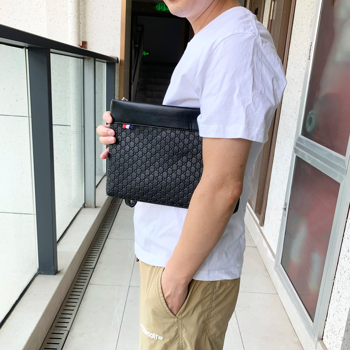 A person holds a black PU leather clutch bag for phone and card storage in a hallway setting.