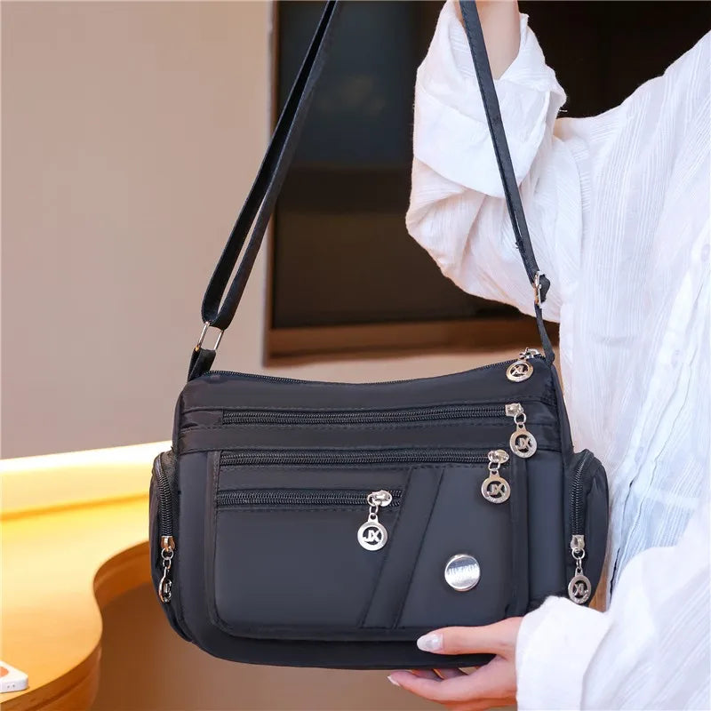 A woman holds a black waterproof nylon crossbody tote bag against a white shirt.