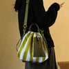 A olive green and white striped insulated lunch bag with an adjustable strap is being held by a person.